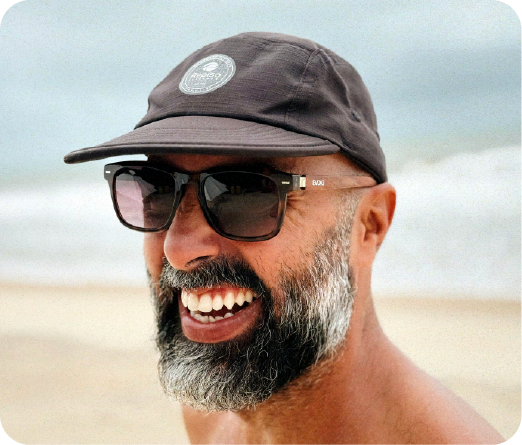 Felipe Repiso sorrindo na praia, de boné e óculos escuros
